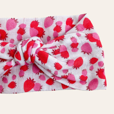 Close up of knotted scarf in gauze fabric. The print is white with pink and red strawberries.